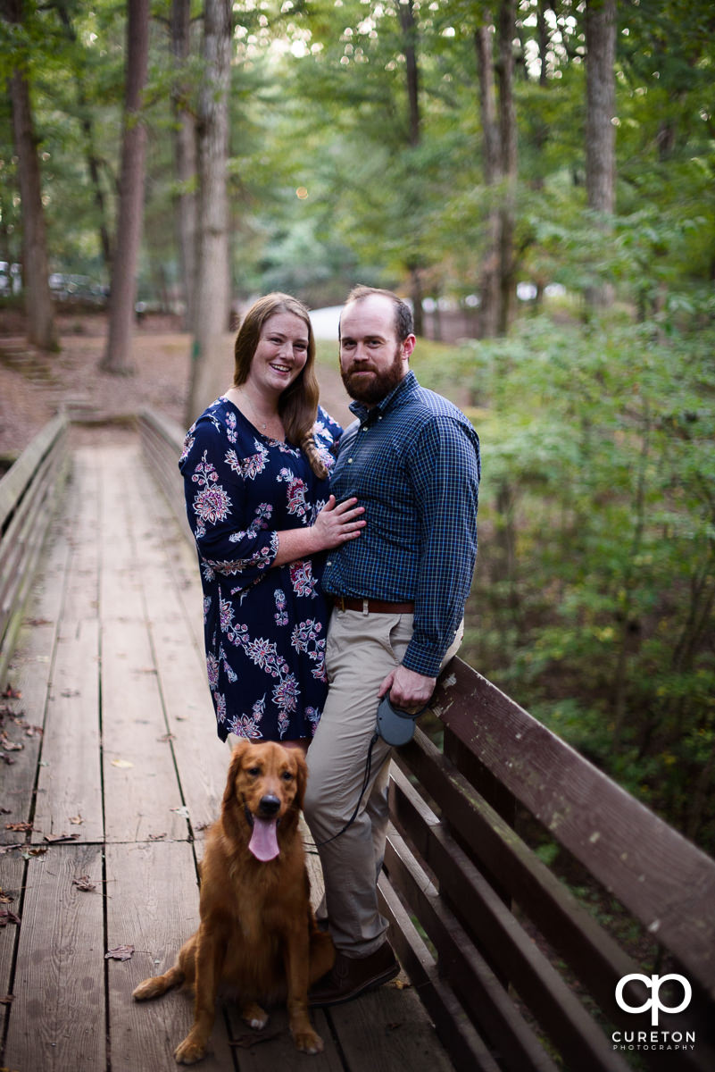 Future bride and groom on a bridge with their dog at Paris Mountain State Park.
