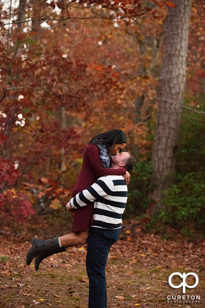 Groom lifting his fiancee with a backdrop of fall colors during their engagement session.