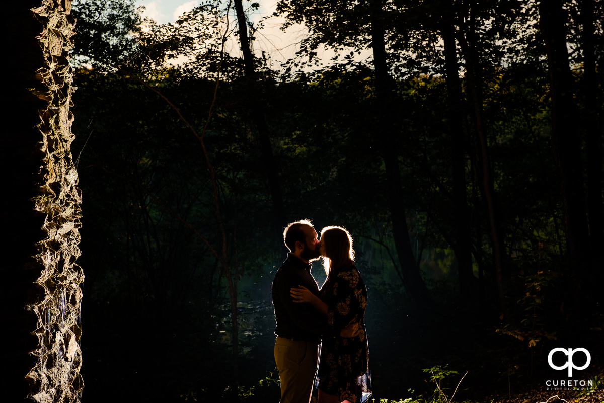 Backlit shot of an engaged couple kissing.