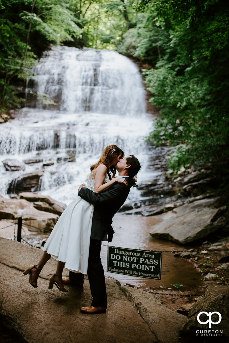 Groom lifting his bride in front of the waterfall after their wedding at Pearson's Falls in Saluda,NC.