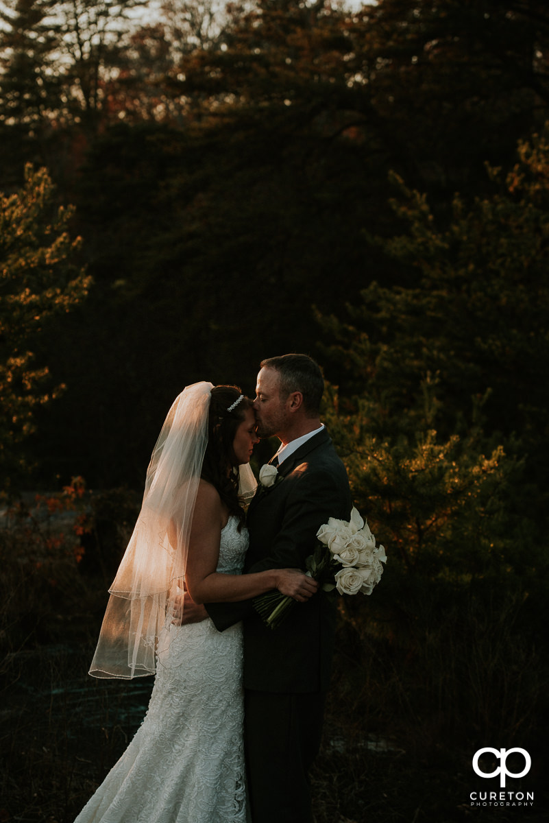 Groom kissing his bride on the forehead in the glow of sunset after their mountain wedding.