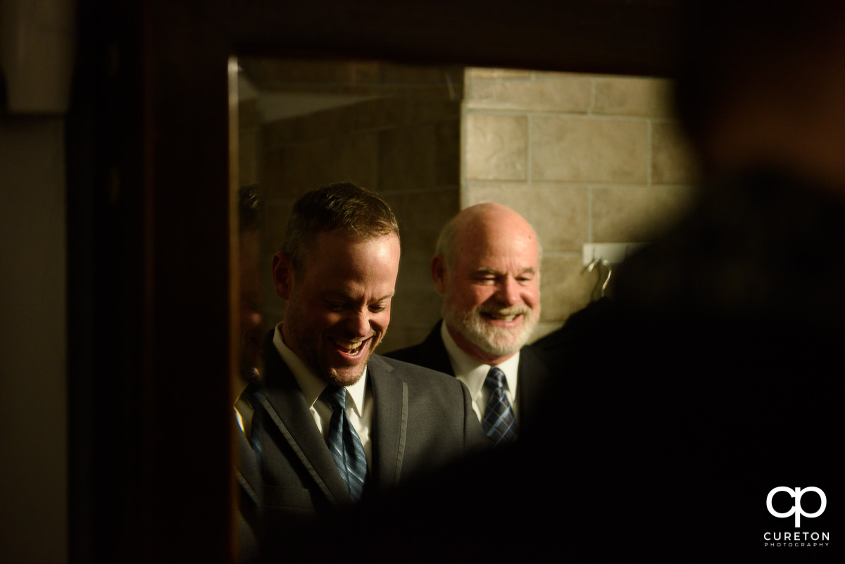 Groom laughing in the mirror as he gets ready.