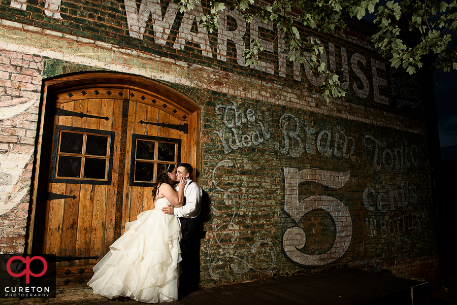 Bride and groom kissing by the Old Cigar Warehouse sign during their wedding reception.