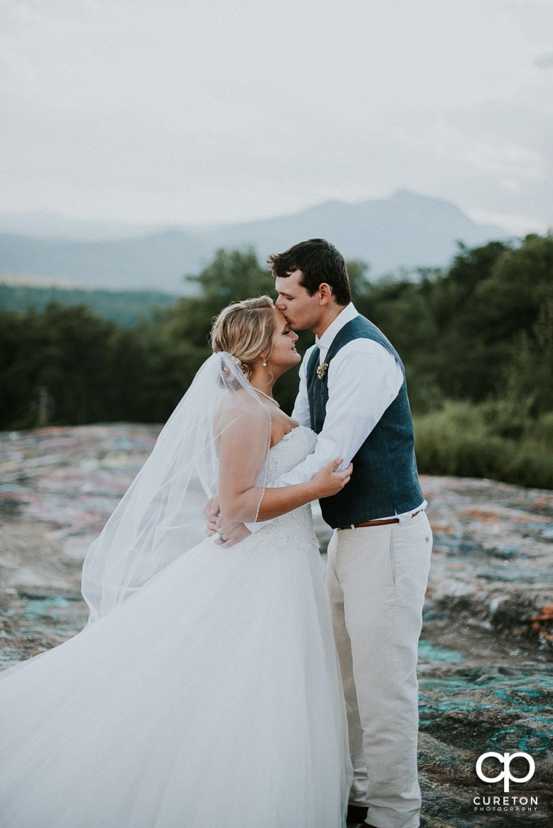 Groom kissing his bride on the forehead.