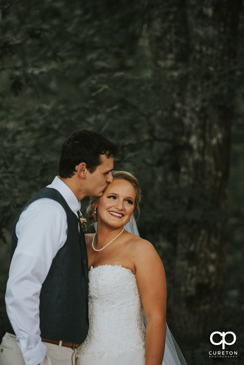 Groom kissing his bride on the forehead.