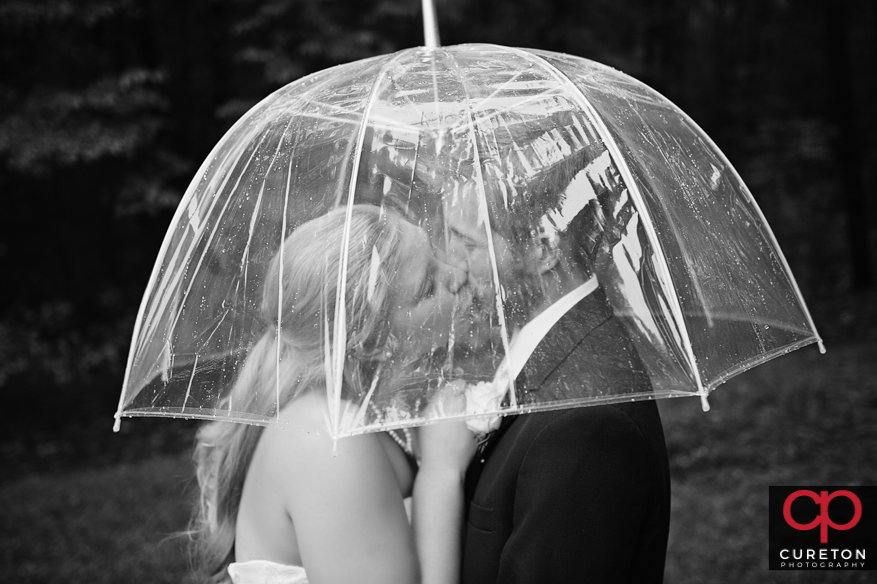Couple kissing under an umbrella during a rain wedding.