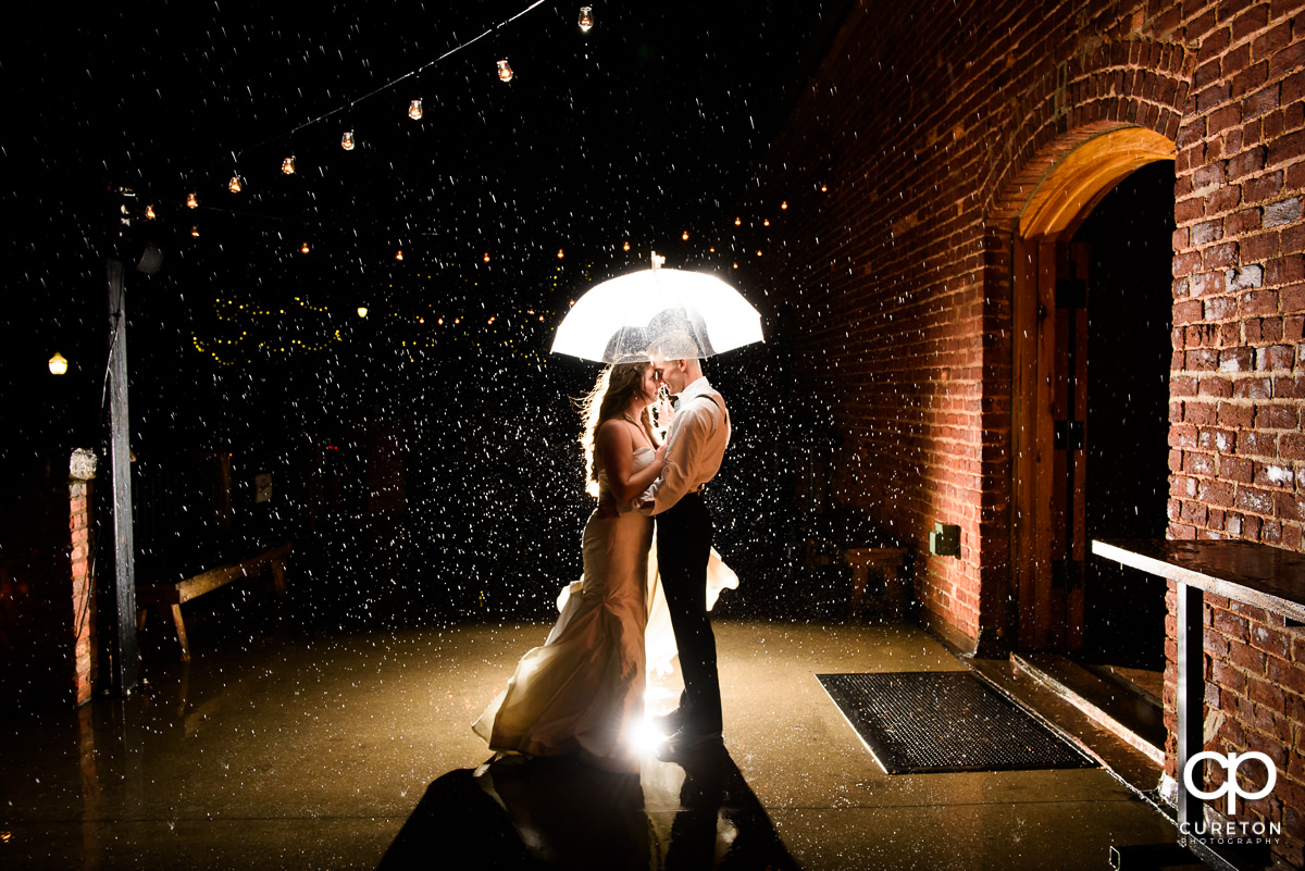 Bride and groom holding an umbrella in the rain at their rainy day wedding at The Old Cigar Warehouse in downtown Greenville,SC.