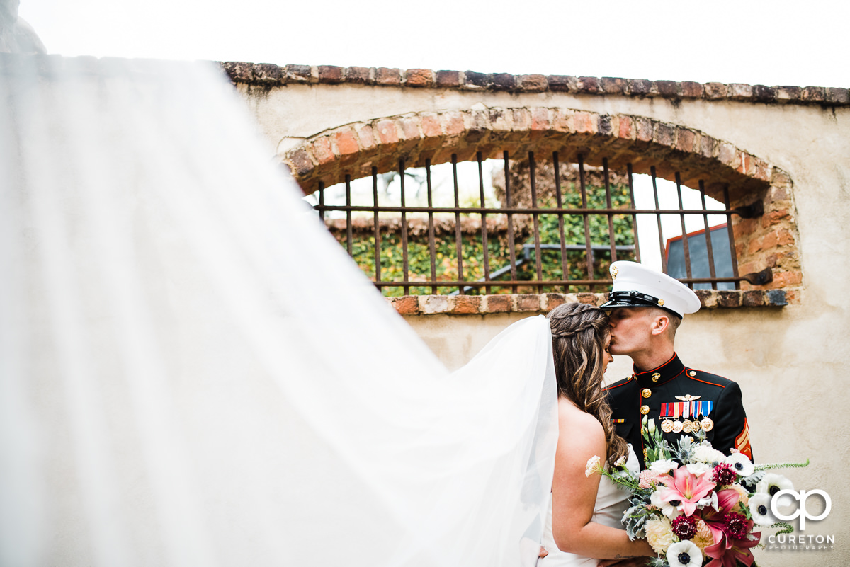 Groom in Marine dress uniform kissing his bride on the forehead at their Old Cigar Warehouse wedding.