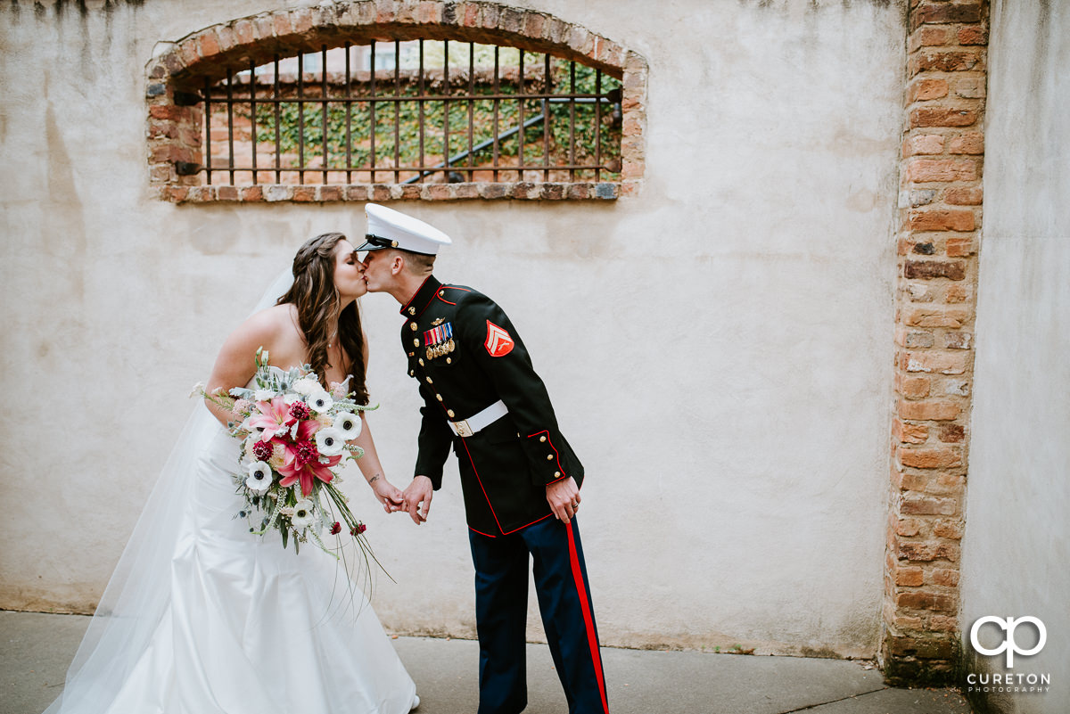 Bride kissing her groom in full Marine dress uniform at The Old Cigar Warehouse.
