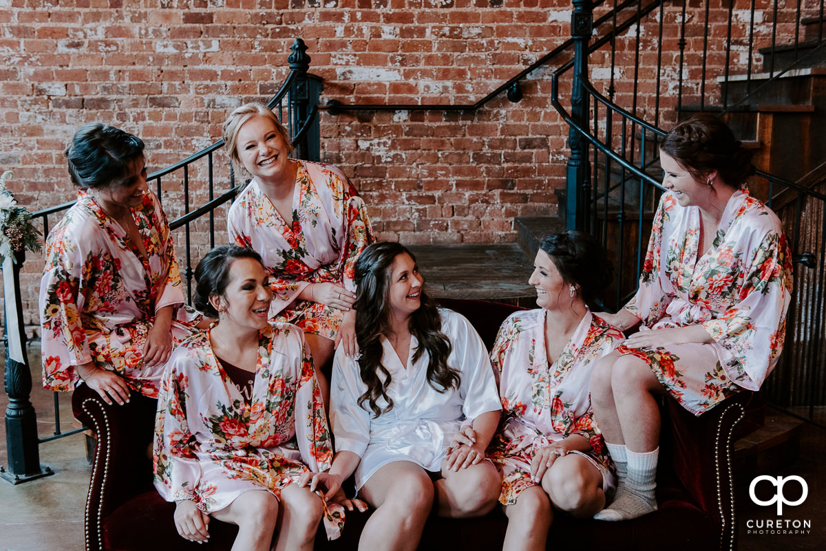 Bride and bridesmaids laughing in robes before the wedding ceremony.