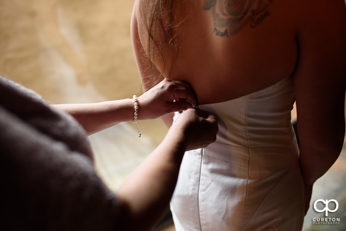 Bride having her dress buttoned.