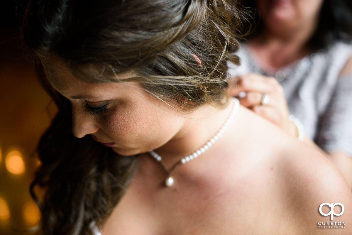 Bride's mother helping the bride put on pearls.