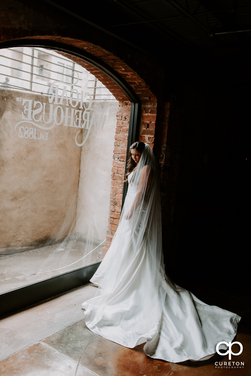 Bride standing in a window in the cellar at The Old Cigar Warehouse in Greenville before her wedding.
