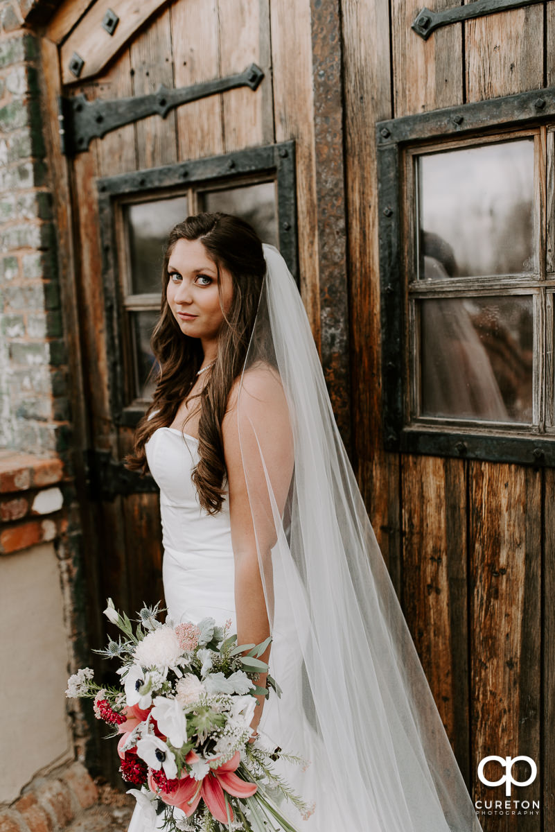 Gorgeous bride holding her bouquet in front of wooden doors outside The Old Cigar Warehouse in Greenville