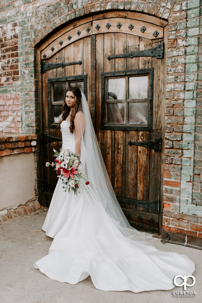 Bride holding her bouquet in front of wooden doors outside The Old Cigar Warehouse in Greenville
