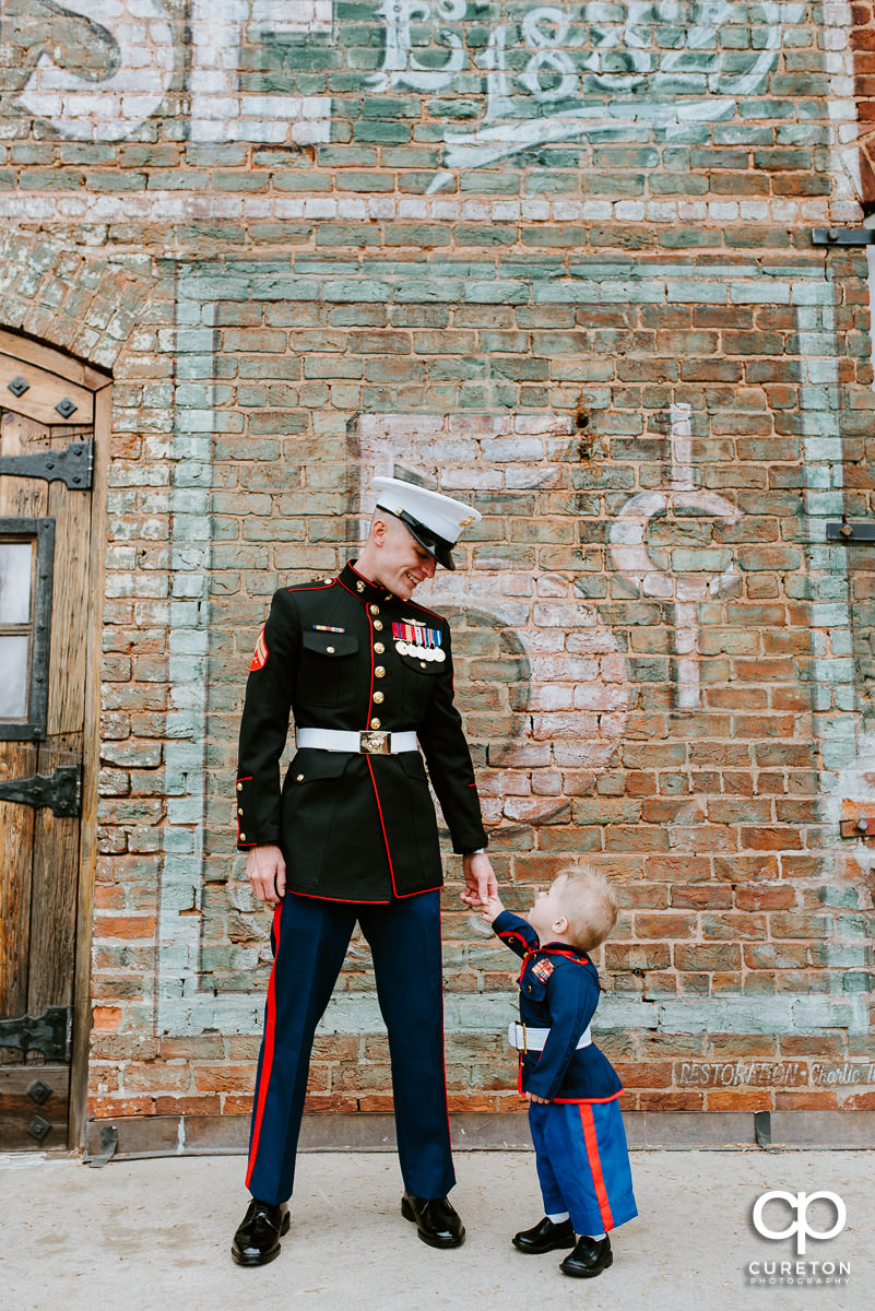 Ring bearer in a Marine uniform looking up to the groom in his Marine Uniform.