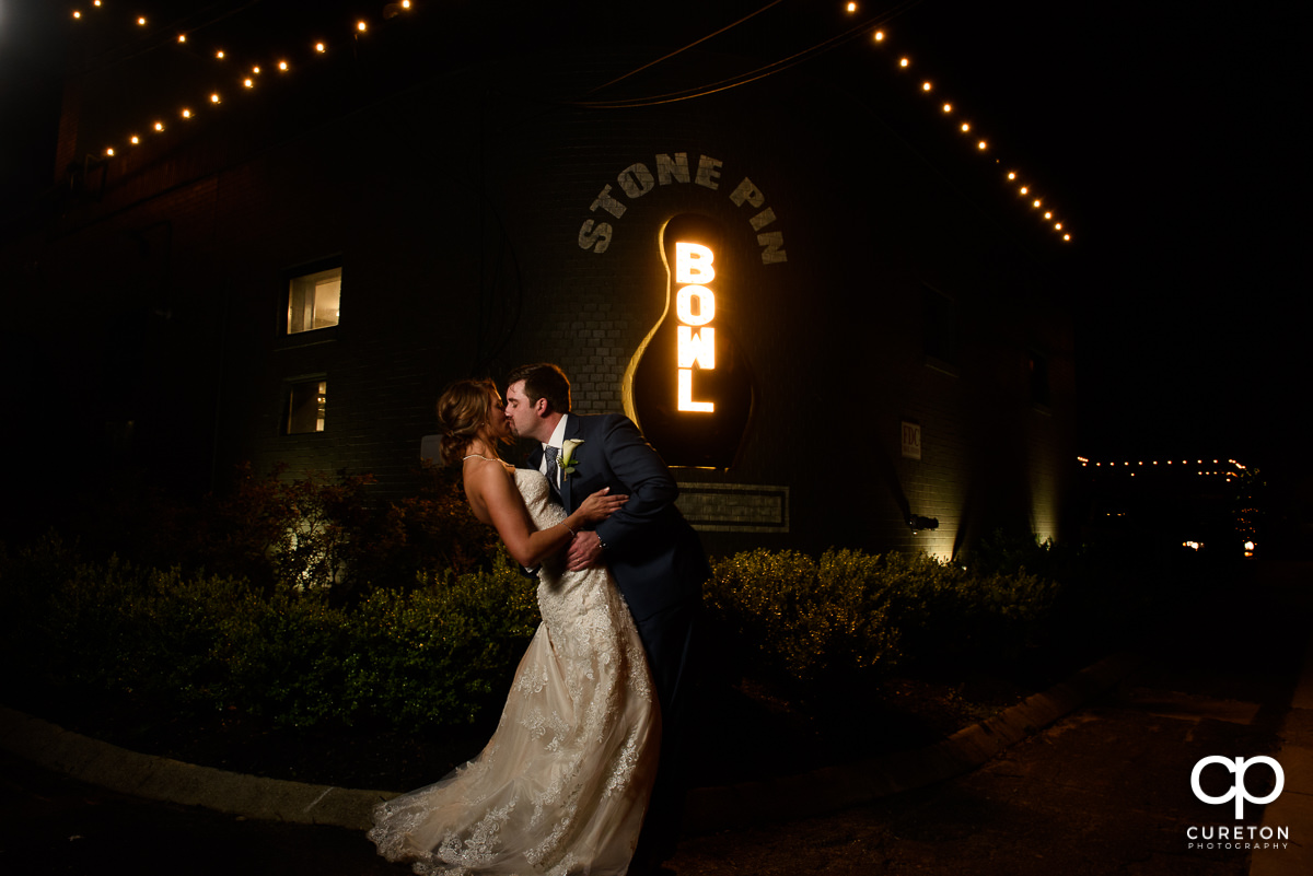 Groom dipping the bride in front of the Stone Pin Bowling sign their Revel Event Center wedding in Greenville,SC.