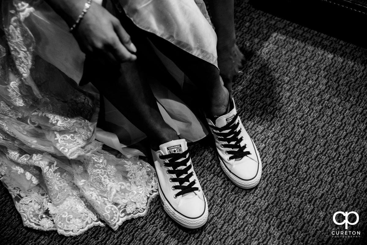 Bride putting on her Chuck Taylor Converse shoes.