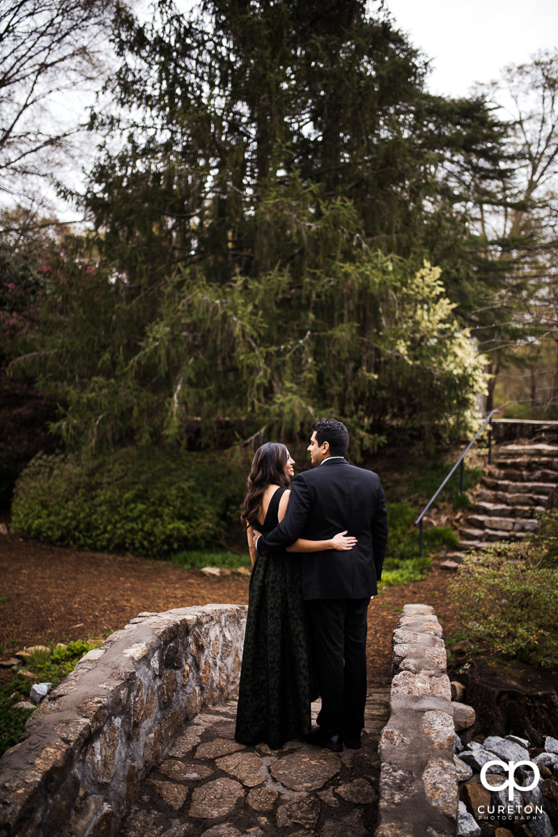 Nicely dressed engaged couple walking over a stone bridge at their engagement session at The Rock Quarry Garden and Cleveland Park in Greenville,SC.