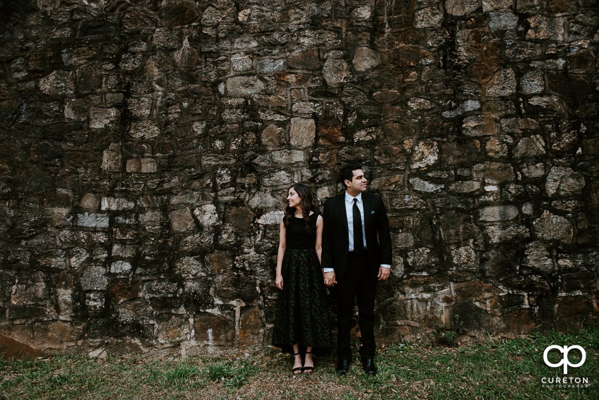 Man and woman standing on a stone wall at their engagement session at The Rock Quarry Garden and Cleveland Park in Greenville,SC.