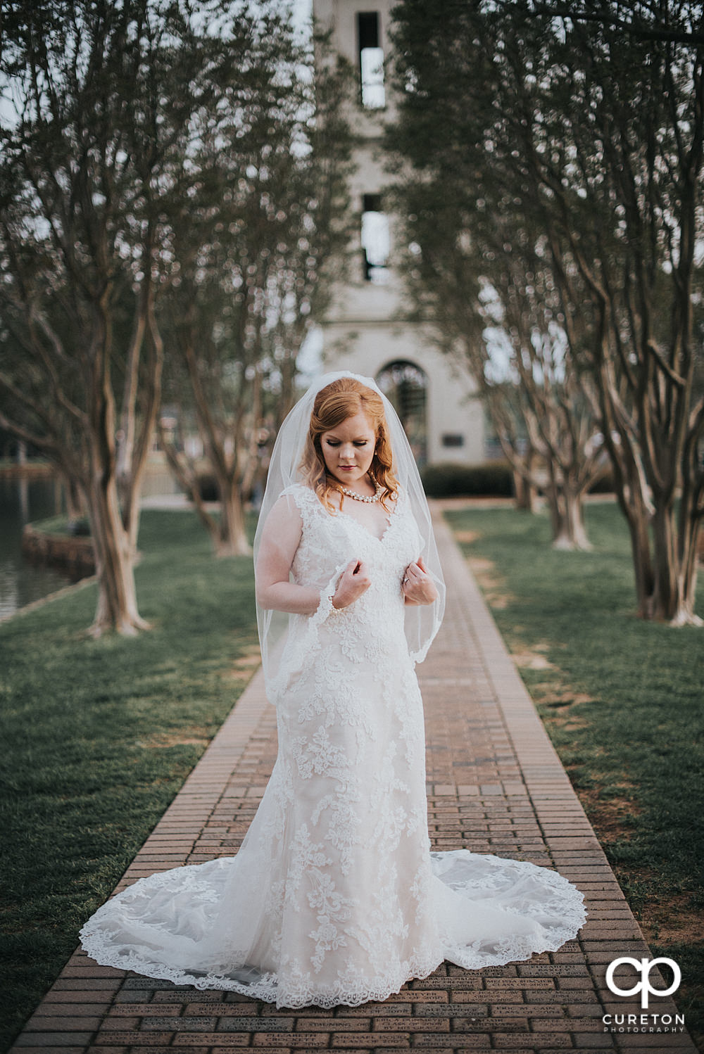 Bride holding her veil in front of the clock tower on the lake during her bridal session at Furman.