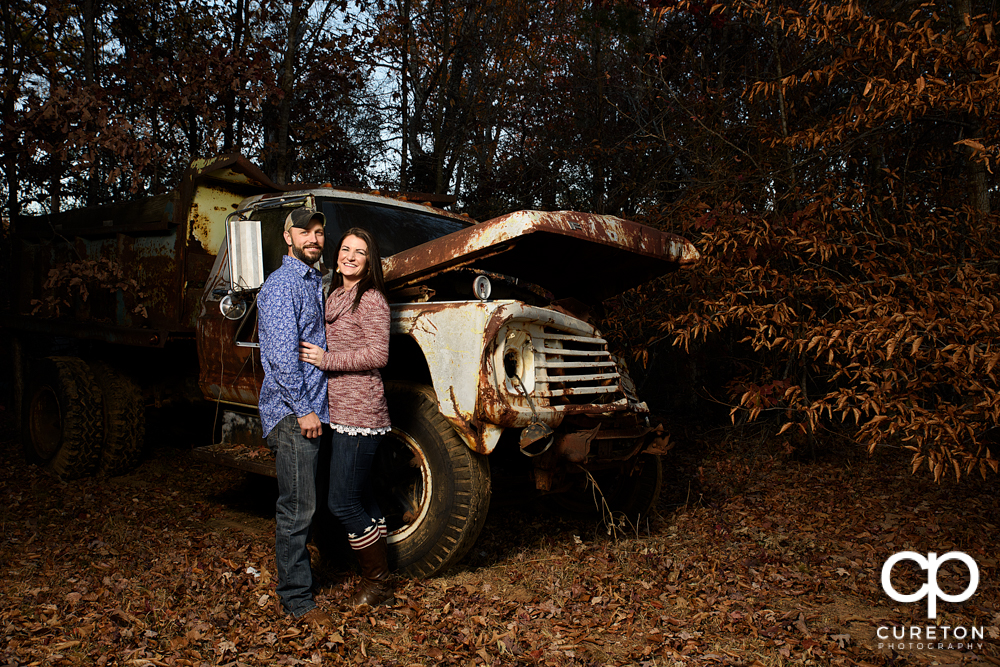 Engaged couple standing near an old rusted truck.