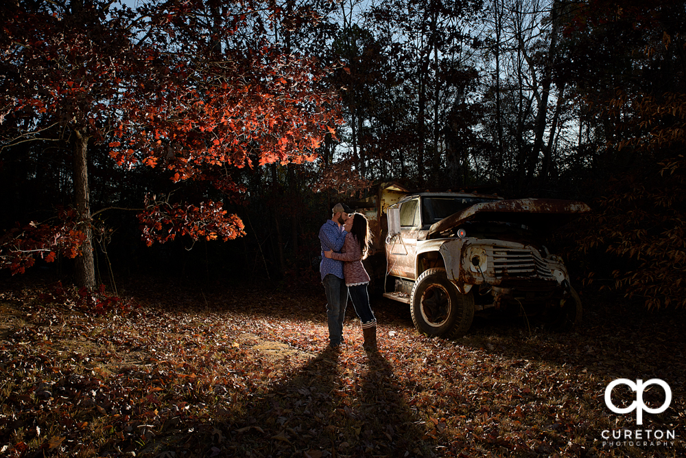 Engaged couple kissing in the fall leaves.
