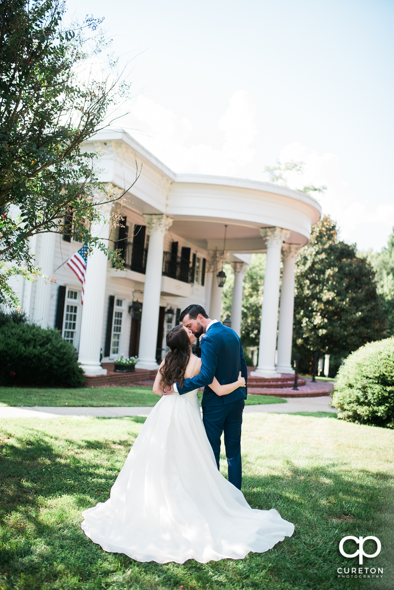 Groom kissing his bride in front of the Southern mansion before their Ryan Nicholas Inn wedding in Mauldin,SC.