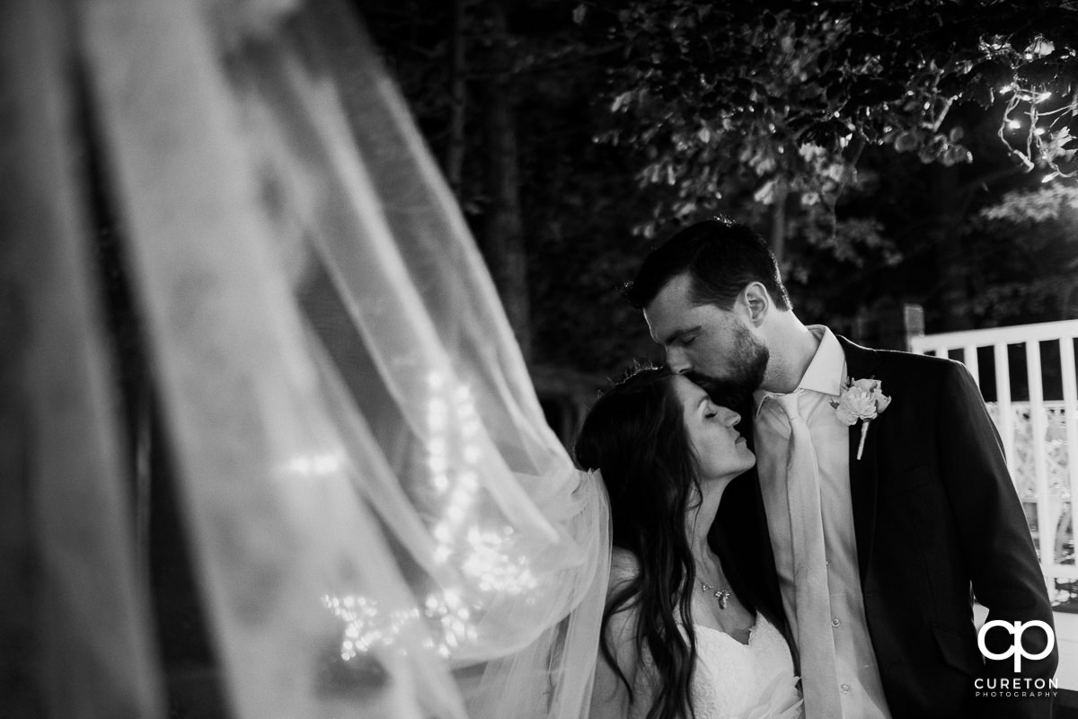 Groom kissing his bride on the forehead.
