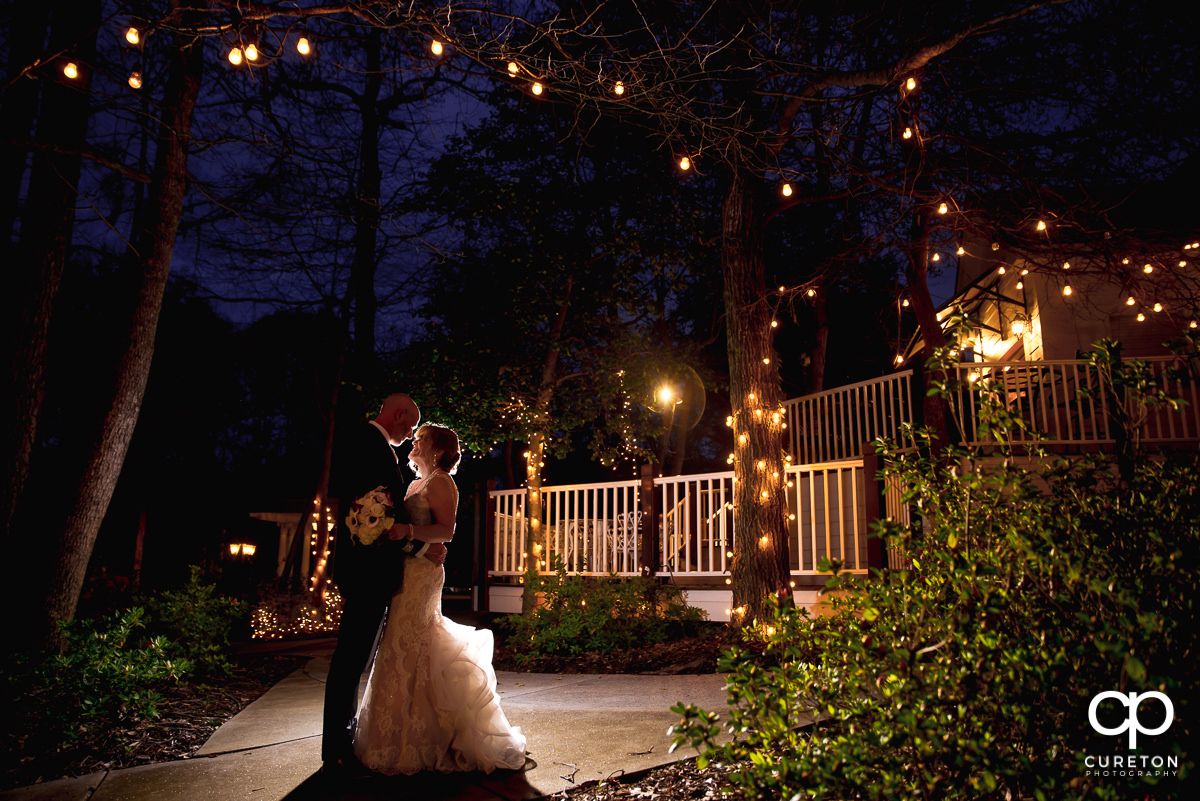 Bride and groom cuddling at twilight surrounded by twinkle lights during their Ryan Nicholas Inn wedding in Mauldin,SC.