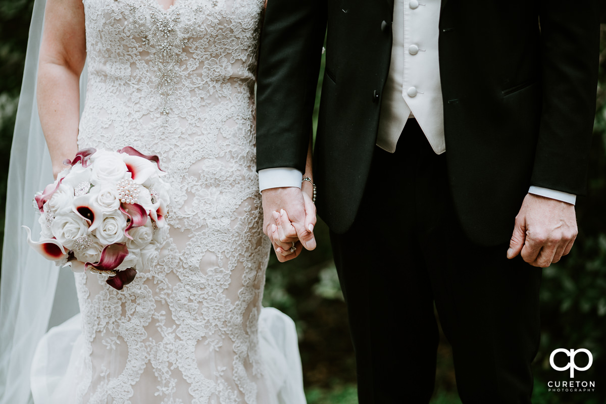 Closeup of a bride and groom holding hands.