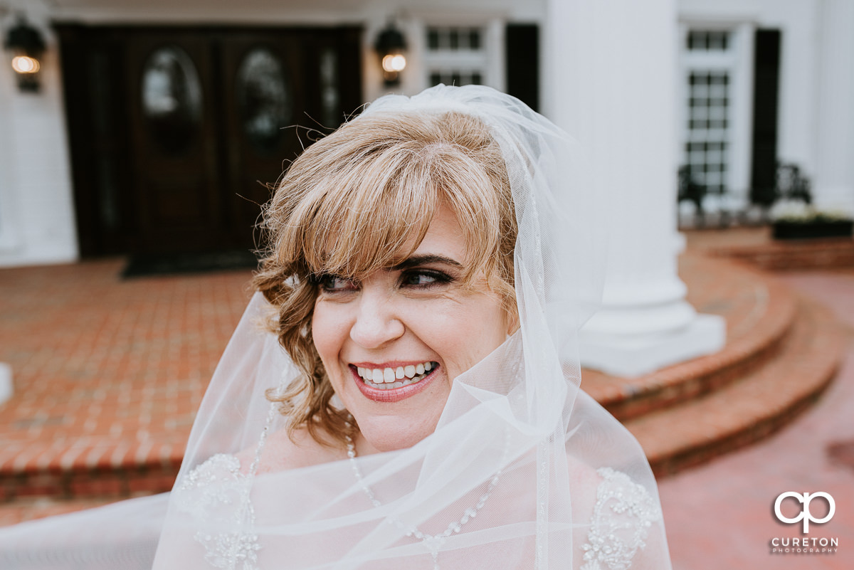 Bride smiling as her veil blows in the wind.