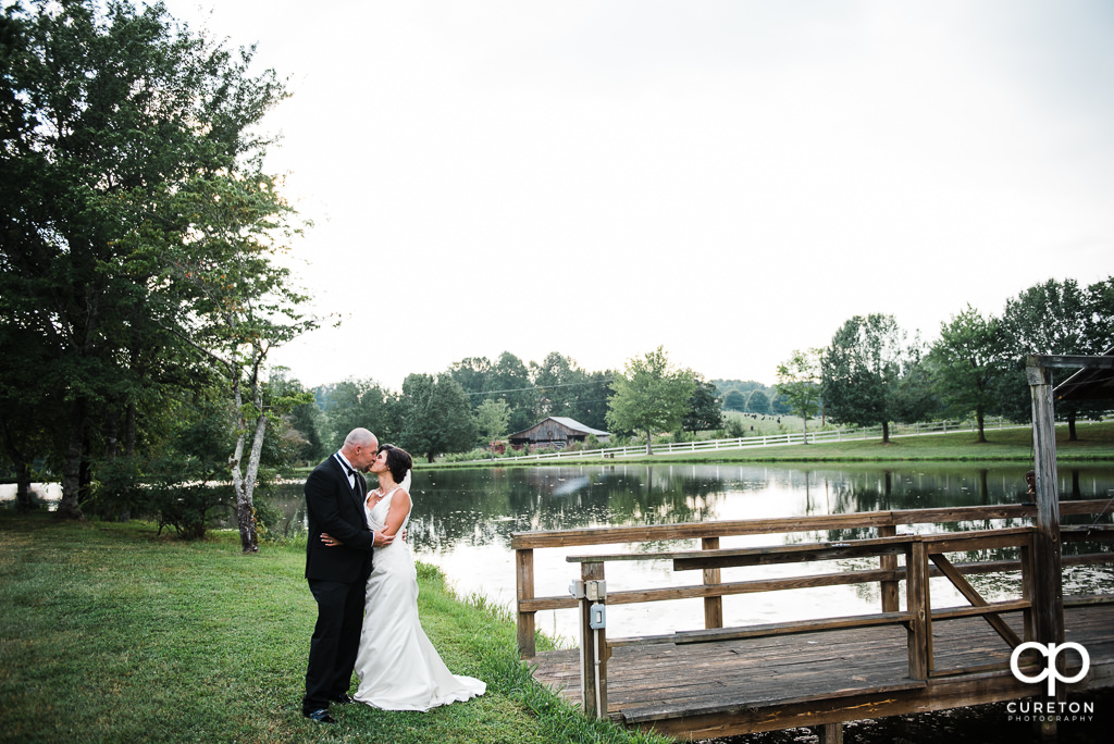 Bride and groom kissing near the dock on the lake at South Wind Ranch, a wedding venue in Travelers Rest SC.