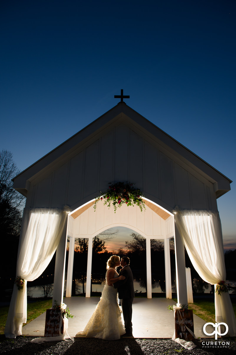 Bride and groom kissing underneath the outdoor chapel at sunset during their South Wind Ranch wedding in Travelers Rest,SC.