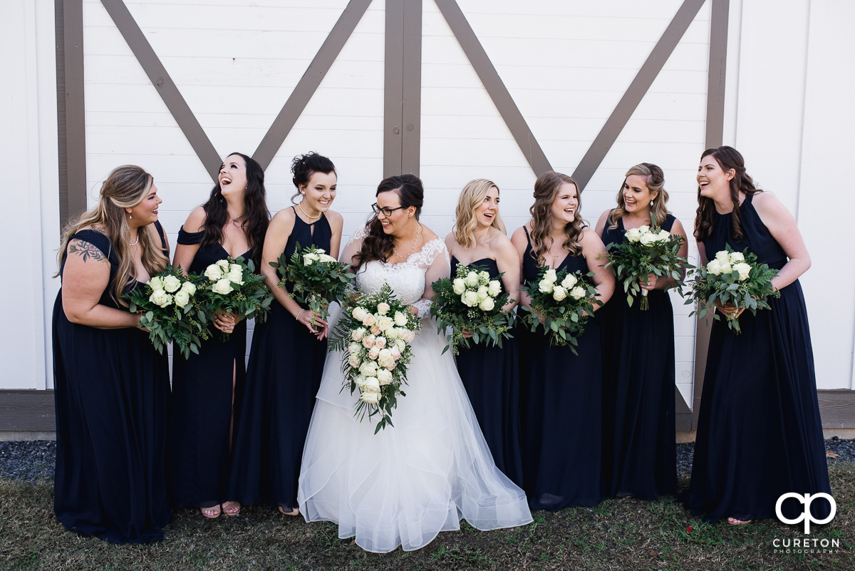 Bride laughing with her bridesmaids in front of white barn doors.