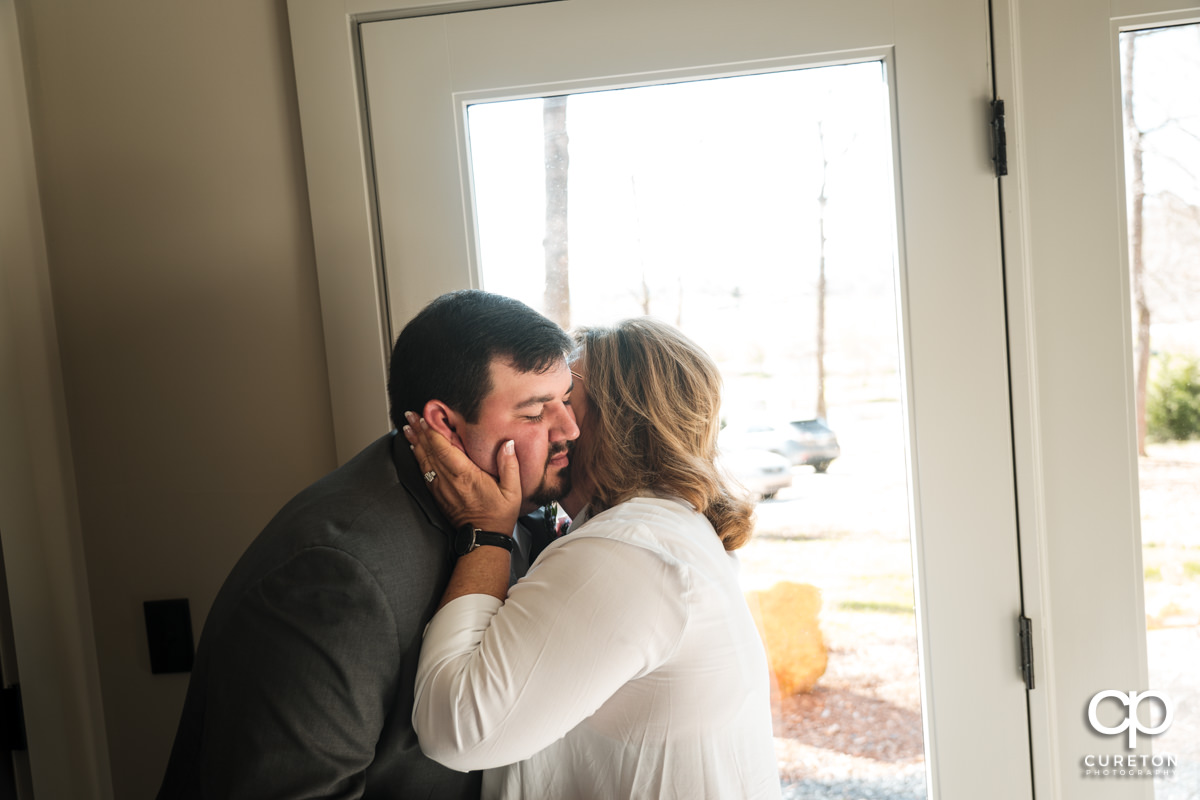 Groom's mom kissing her son on the cheek as she helps him get ready.