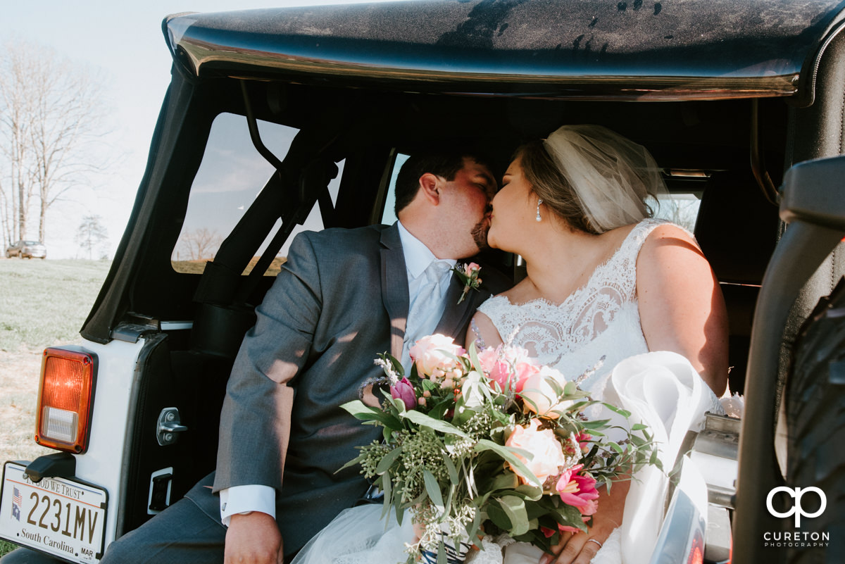 Bride and groom kissing in the back of a jeep.