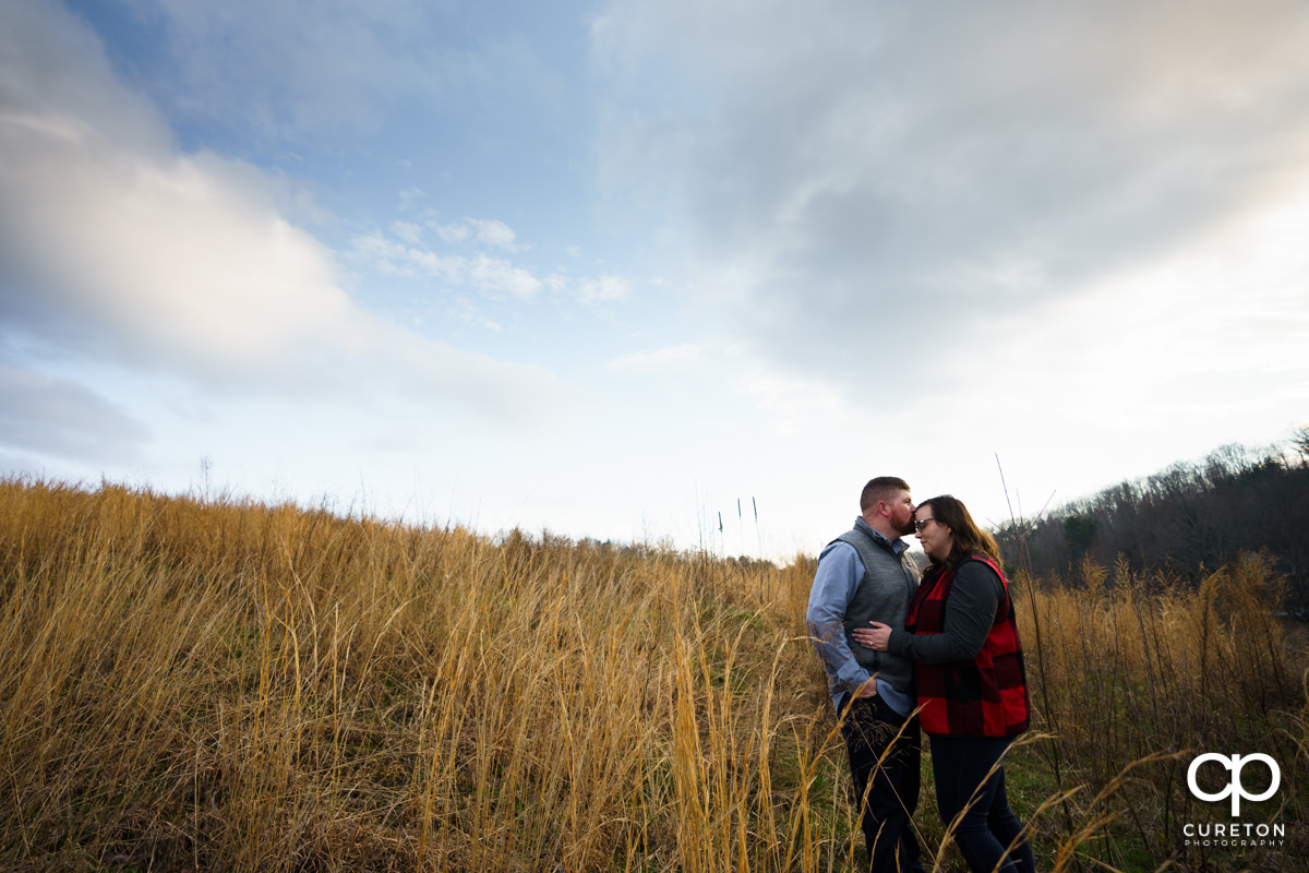Man kissing his fiancee on the forehead durin their engagement session at South Wind Ranch.
