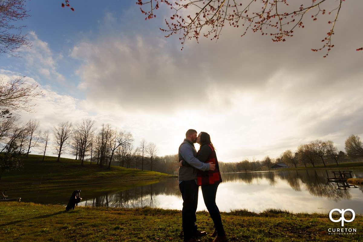 Man kissing his future bride by the lake at South Wind Ranch at an engagement session.