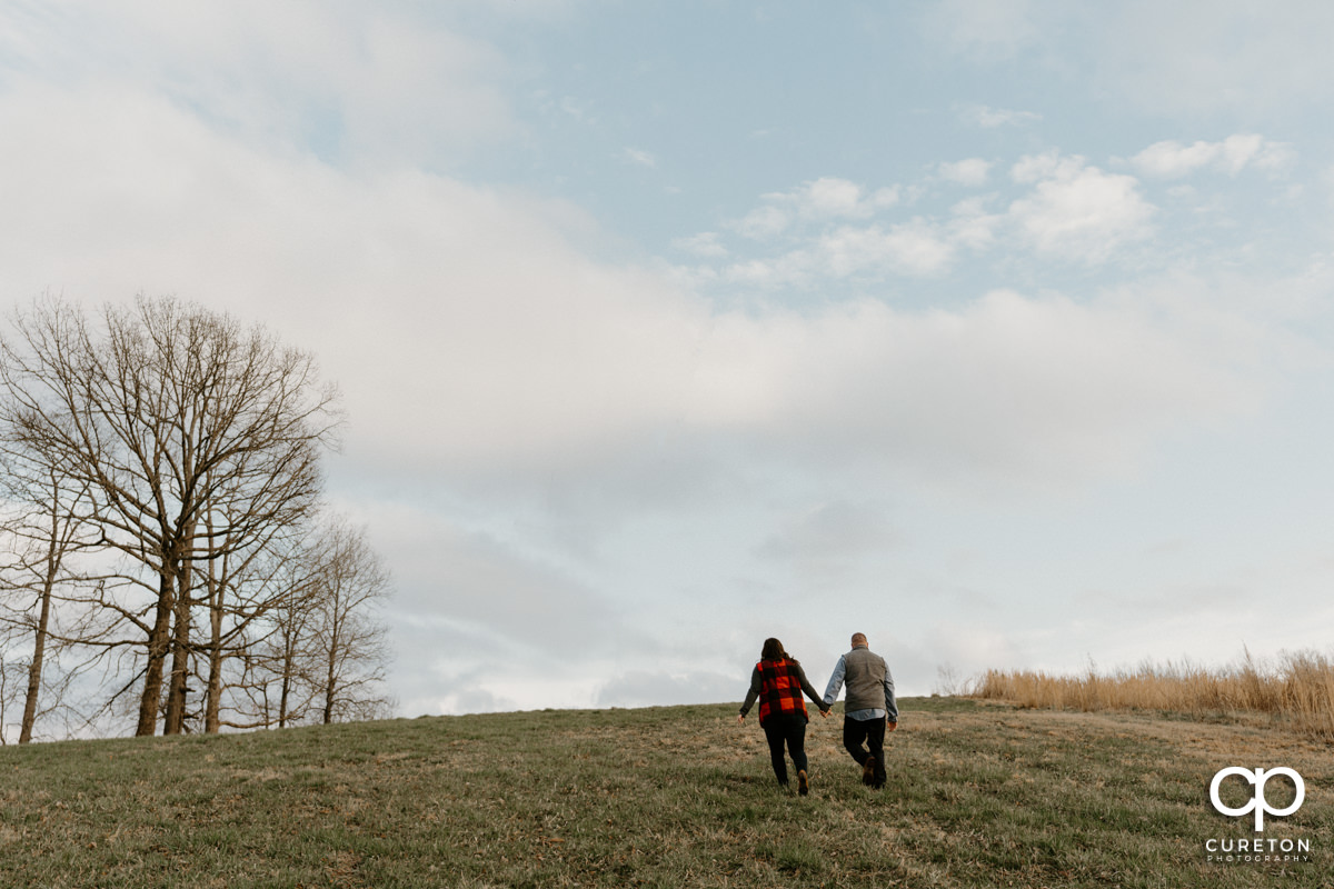 Engaged couple walking in the meadow during a pre wedding South Wind Ranch engagement session in Travelers Rest,SC.