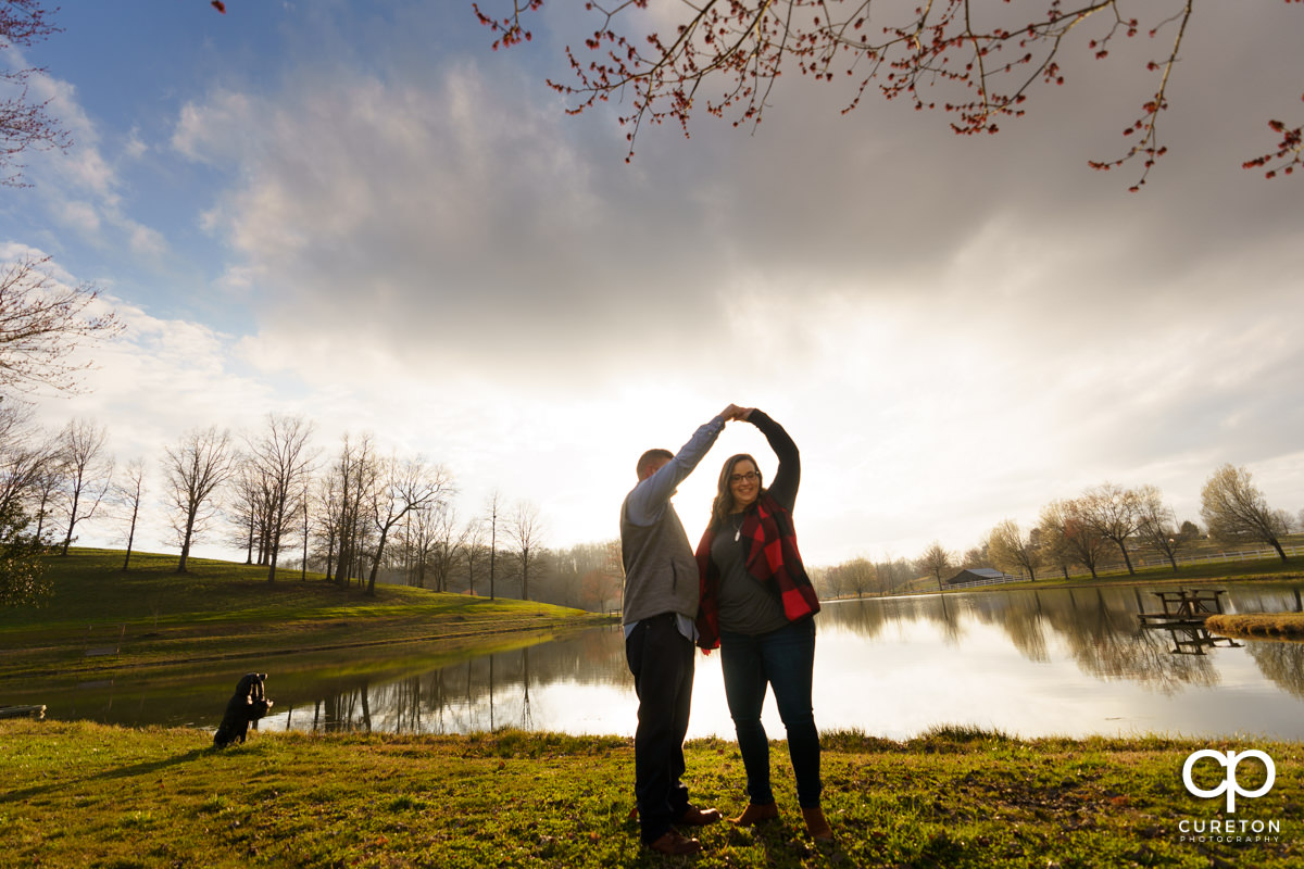 Engaged couple dancing in front of a lake.