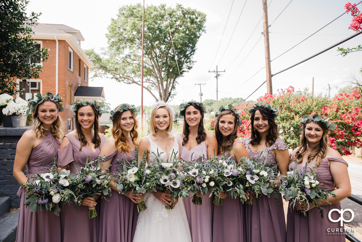 Bride and bridesmaids in purple dresses holding flowers.