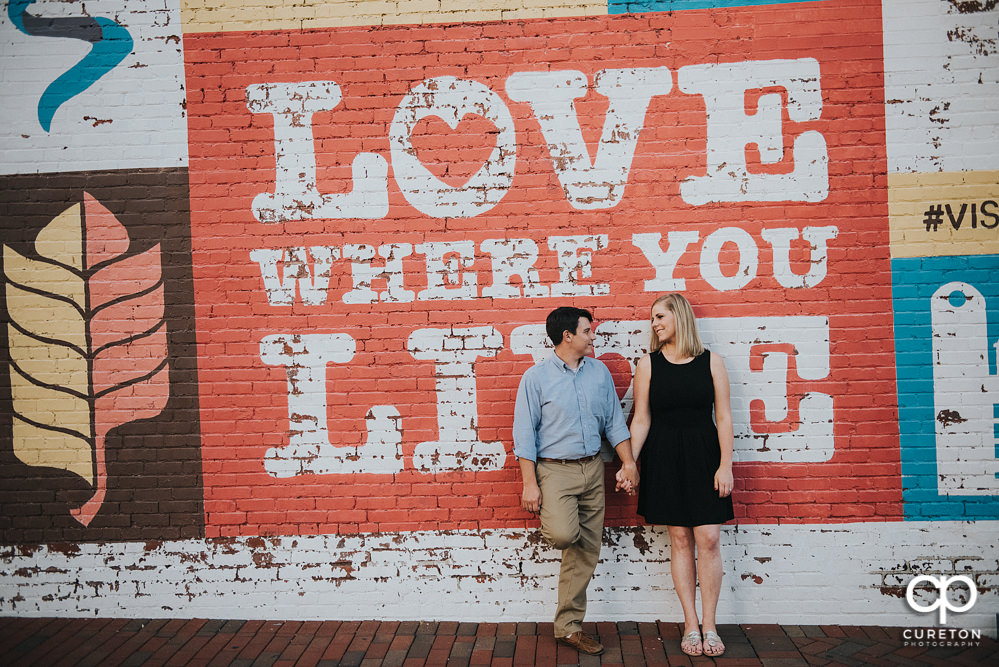 Engaged couple leaning on a wall in downtown Spartanburg,SC.