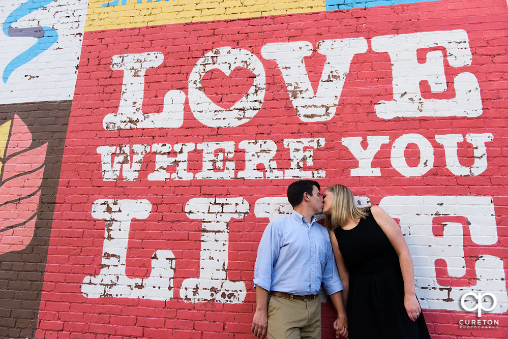 Engaged couple leaning on a wall in downtown Spartanburg,SC.