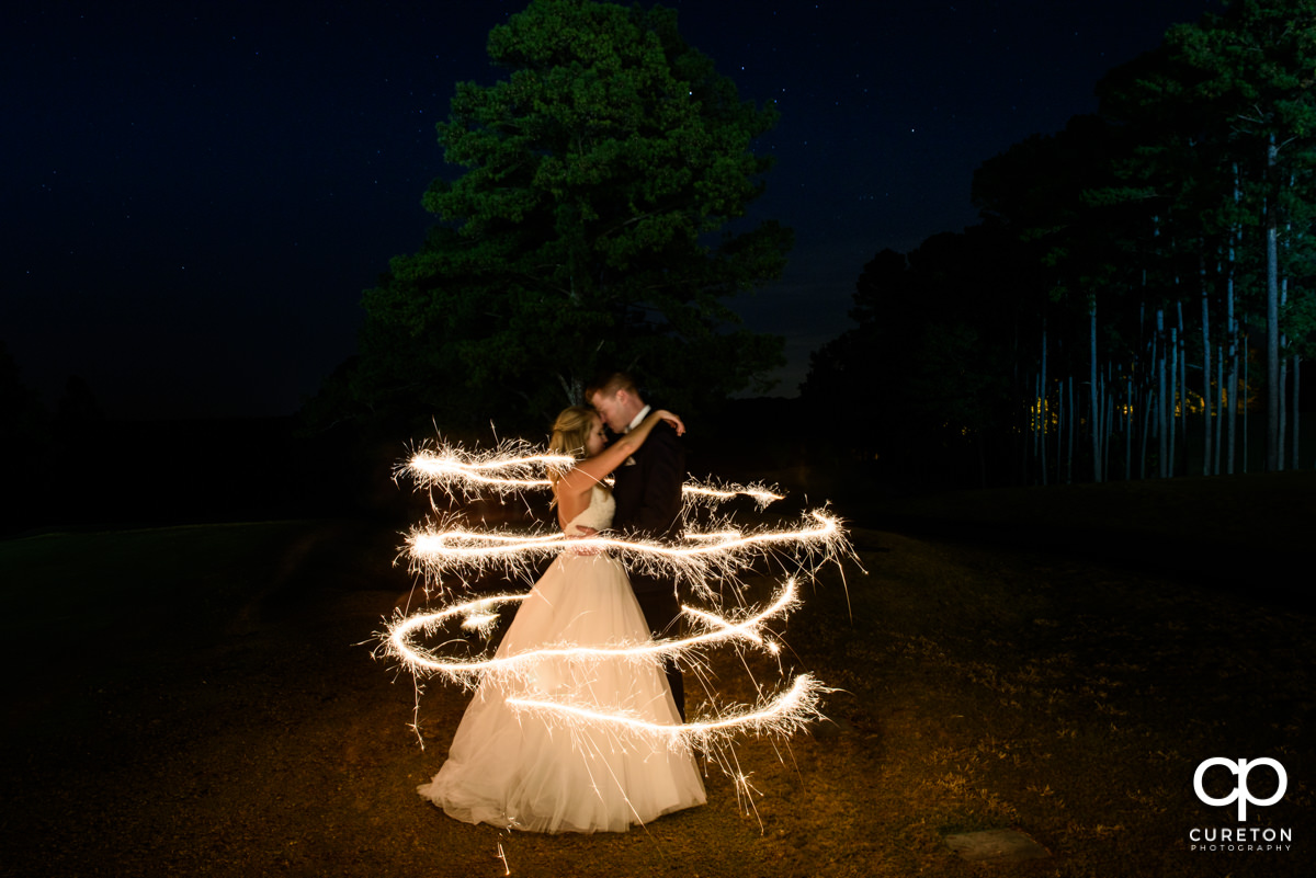 Bride and groom surrounded by sparks from a sparkler at night.
