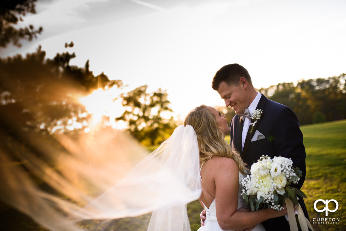 Groom and bride hugging during golden hour as her veil blows in the wind.