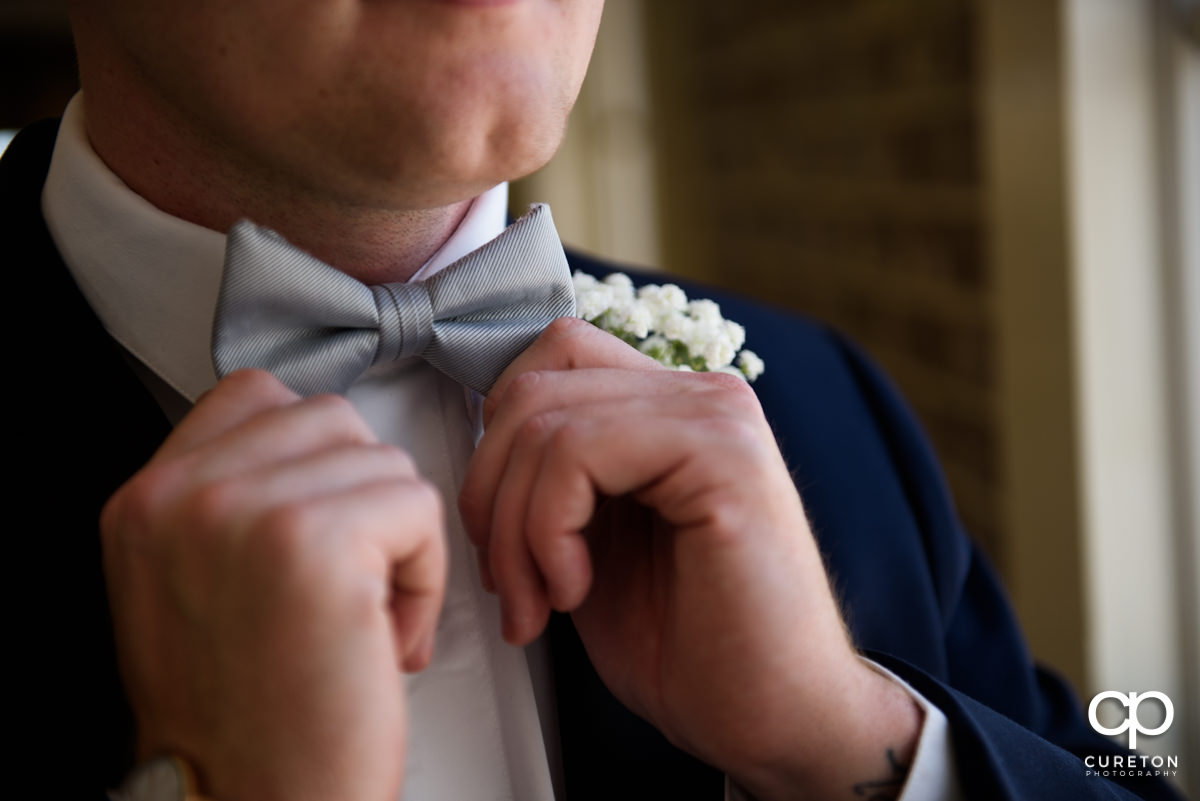 Groom fixing his silver bowtie on his wedding day.