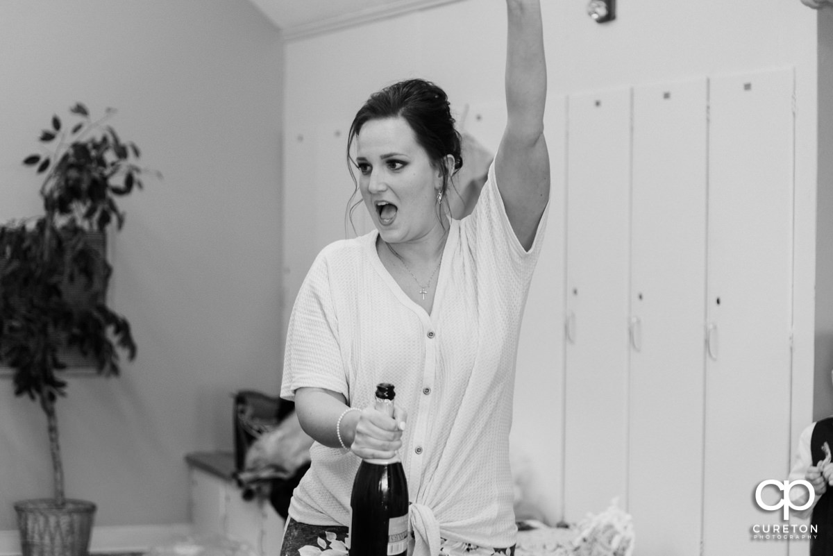 Bridesmaid popping the cork on a bottle of champagne in the bridal suite.