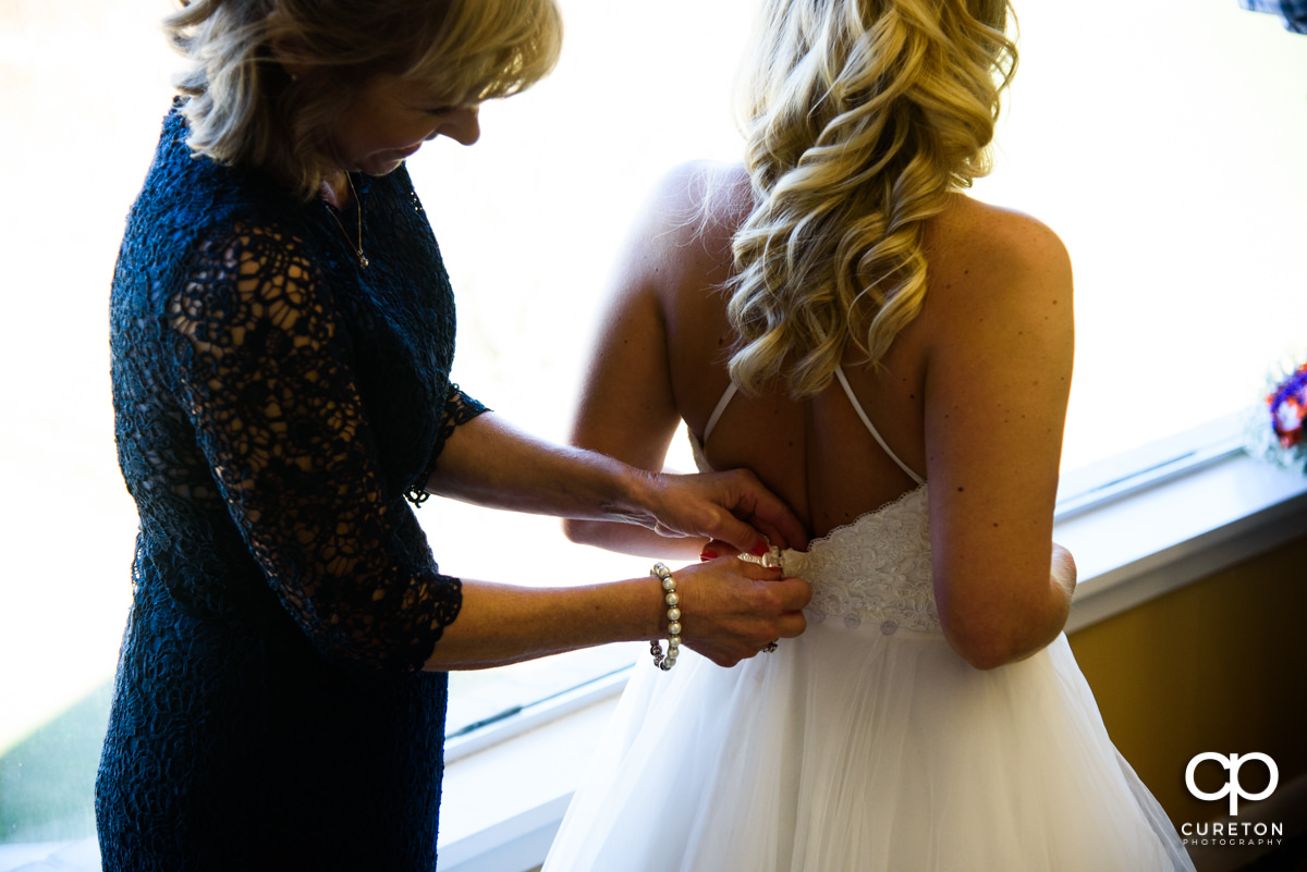 Bride's mother helping her daughter into her wedding dress.