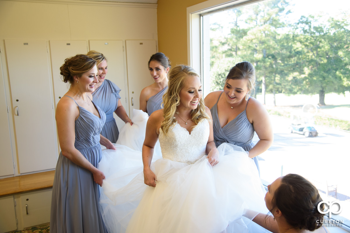 Bride laughing with her bridesmaids as they help her into her gown.